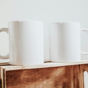 Two minimalist white ceramic mugs on a wooden box, perfect for coffee or tea.
