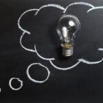 Light bulb laying on chalkboard with drawn thought bubble, symbolizing creative ideas.