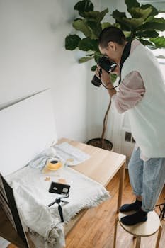 Side view of dark haired woman with photo camera standing on chair while taking photo of cup of coffee on table with cloth